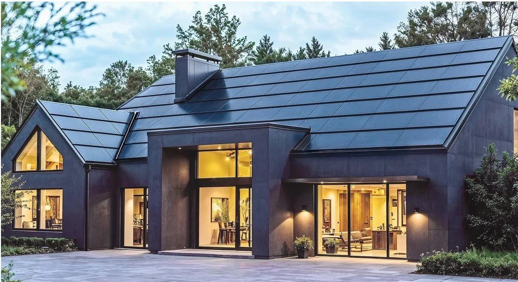 A modern home at dusk under a full Quad+ solar roof, windows lit from within